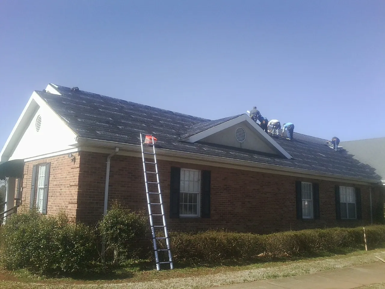 Crew tearing shingles off a brick ranch roof with a ladder set — Metal Roof Repair work by our crew in Hopewell Junction