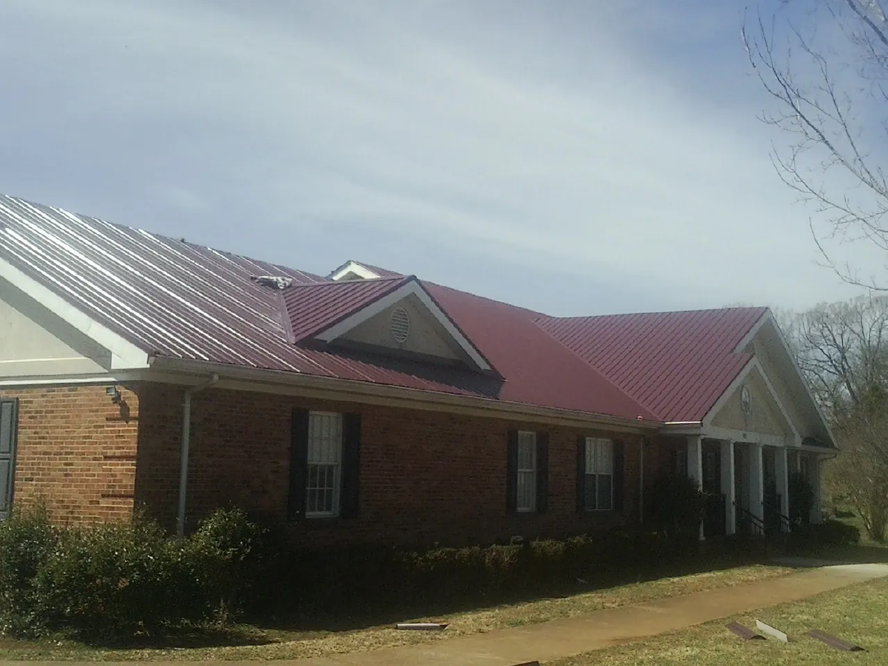 Red metal roof with gabled entries on a long brick building, from a Hail Damage Roof Repair job in Hopewell Junction