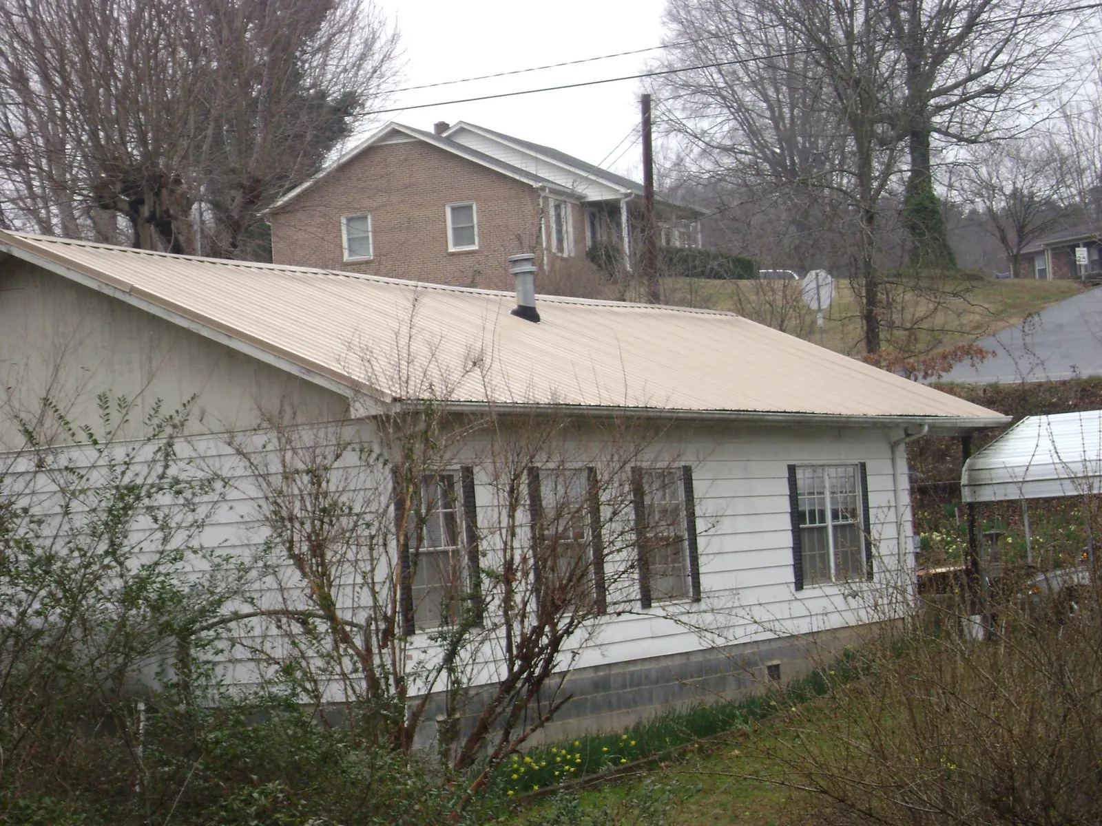 Tan metal roof on a white sided house set into a hillside — Commercial Roofing by Roofing Brothers in Hopewell Junction